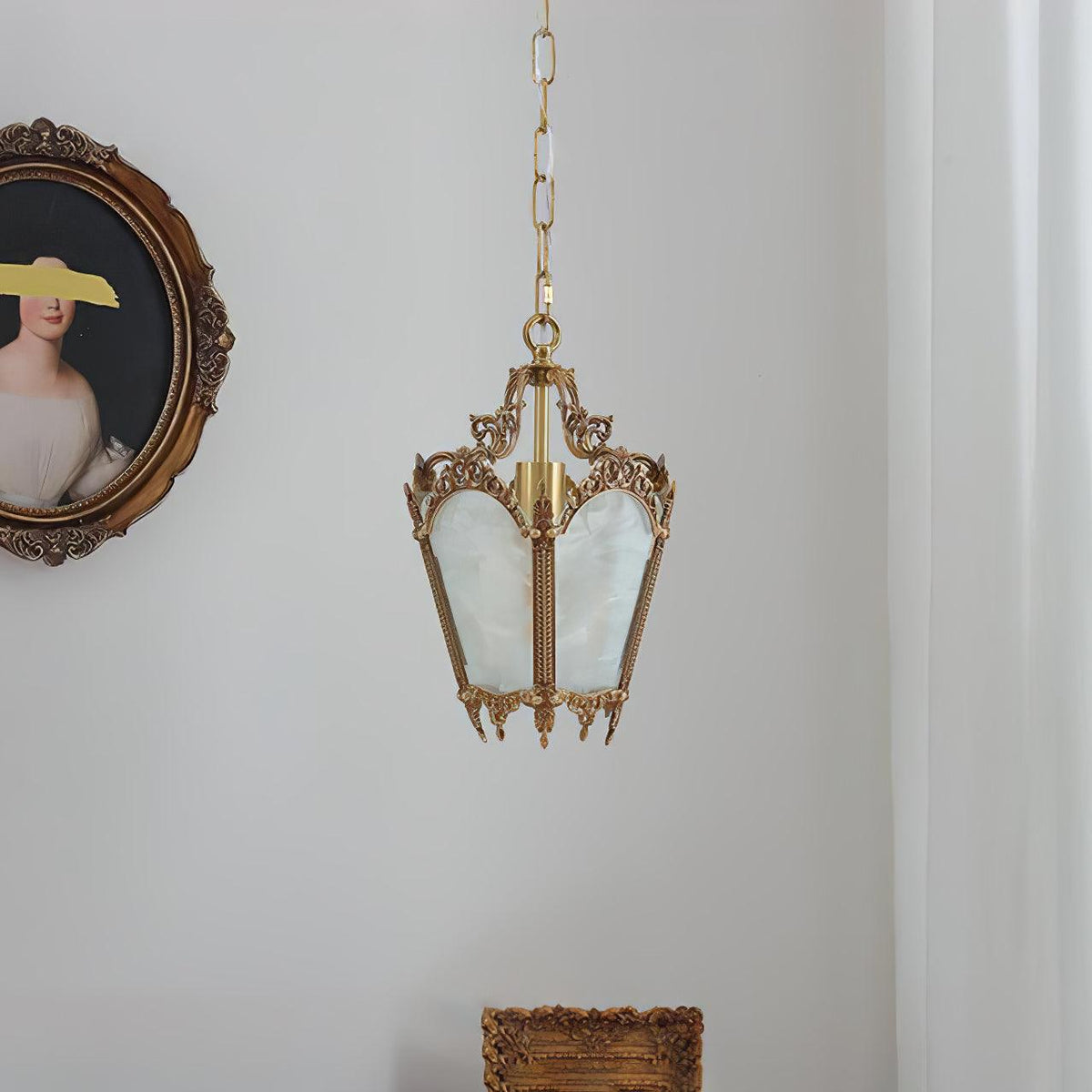 Unlit Clérachic brass lantern pendant on a chain, hung on a pale wall with a portrait and a gilt frame.