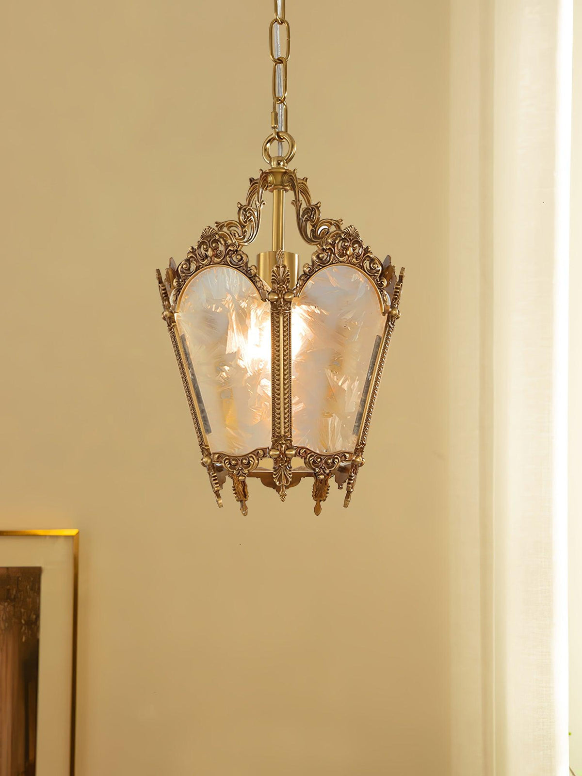 Clérachic brass lantern pendant against a warm cream wall, a framed picture and a curtain at the sides.