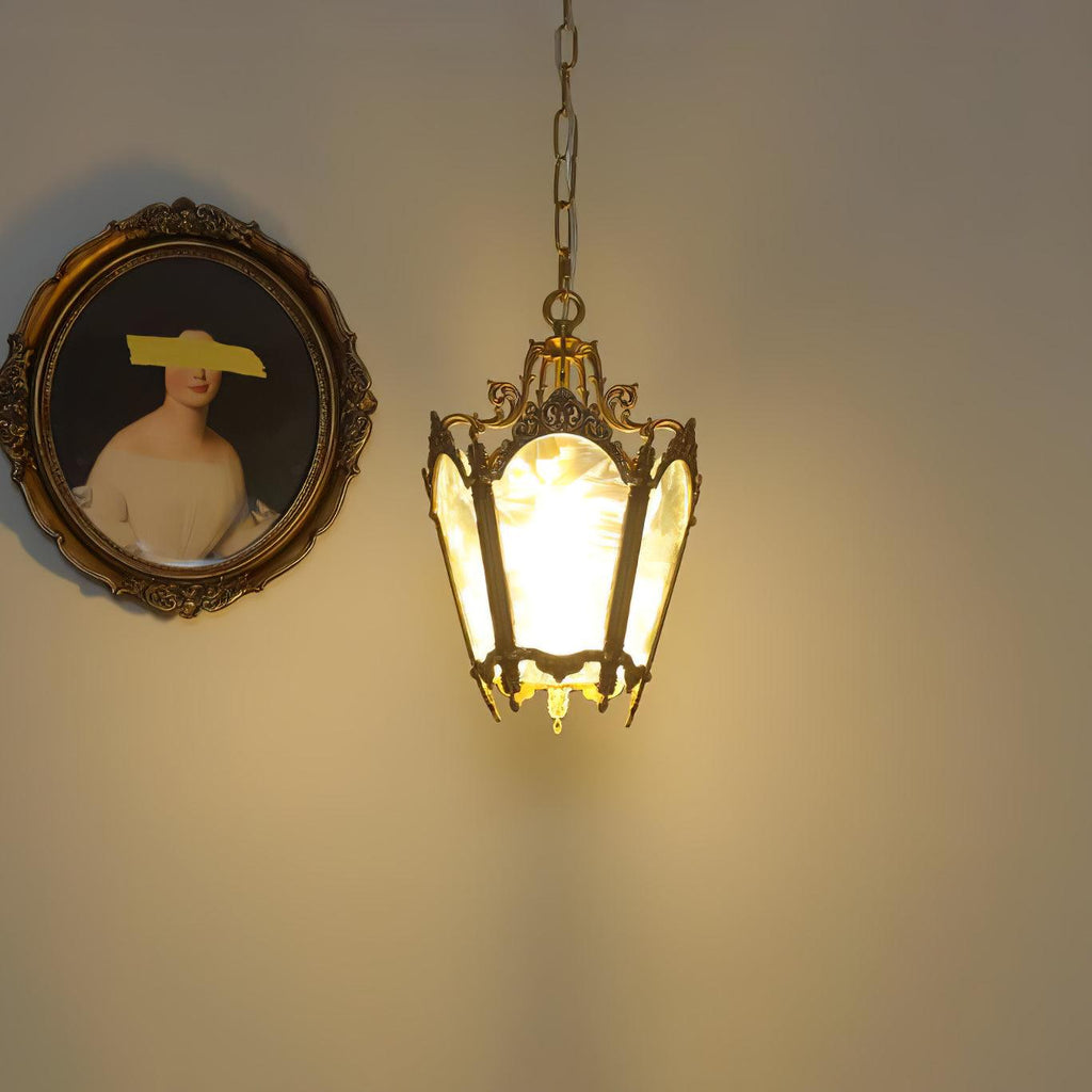 Lit Clérachic lantern pendant glowing warm on a cream wall beside an oval framed portrait.