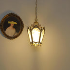 Lit Clérachic lantern pendant glowing warm on a cream wall beside an oval framed portrait.