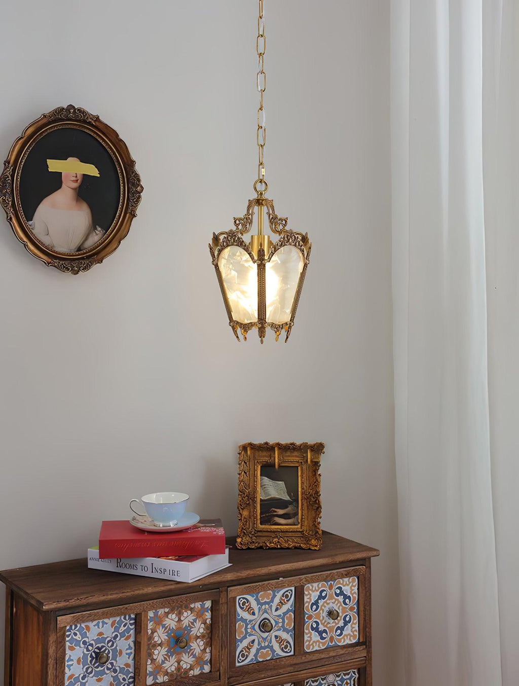 Brass lantern pendant above a painted wooden cabinet with a teacup and a framed picture, a portrait on the wall, from Clérachic.