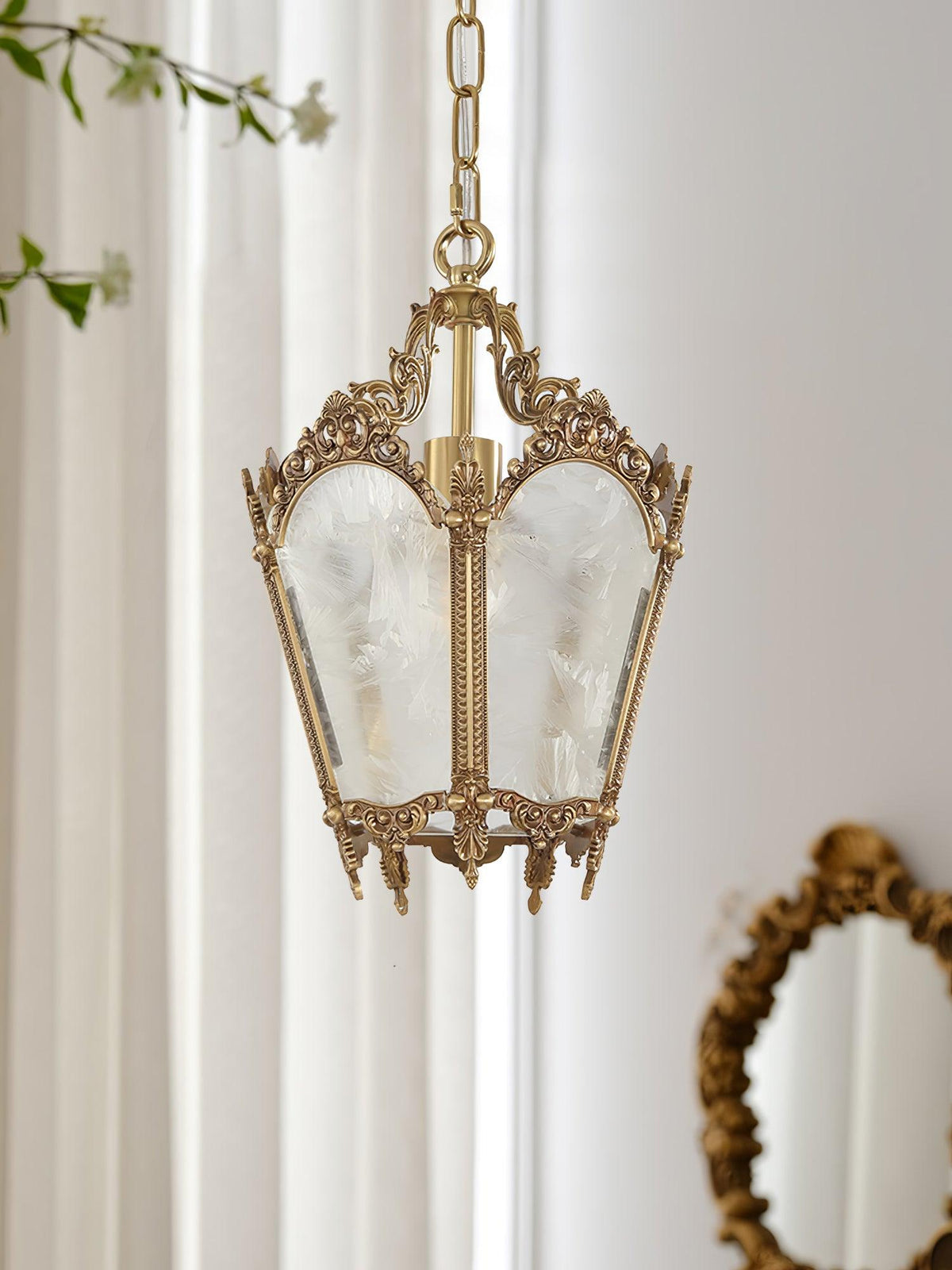Clérachic brass lantern pendant against sheer curtains, a leafy stem above it and a gilt oval mirror below.