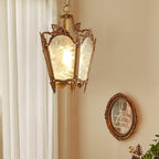 Brass lantern pendant lit beside a sheer curtain, with a small oval frame on the wall behind, from Clérachic.