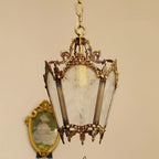 Clérachic brass lantern pendant against a peach wall, in front of a gilt oval portrait, with frosted panes showing.