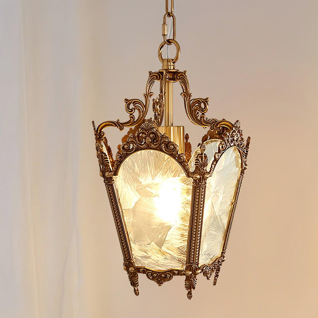 Brass lantern pendant, lit, with an ornate crown and frosted glass, against a soft pink curtain, from Clérachic.