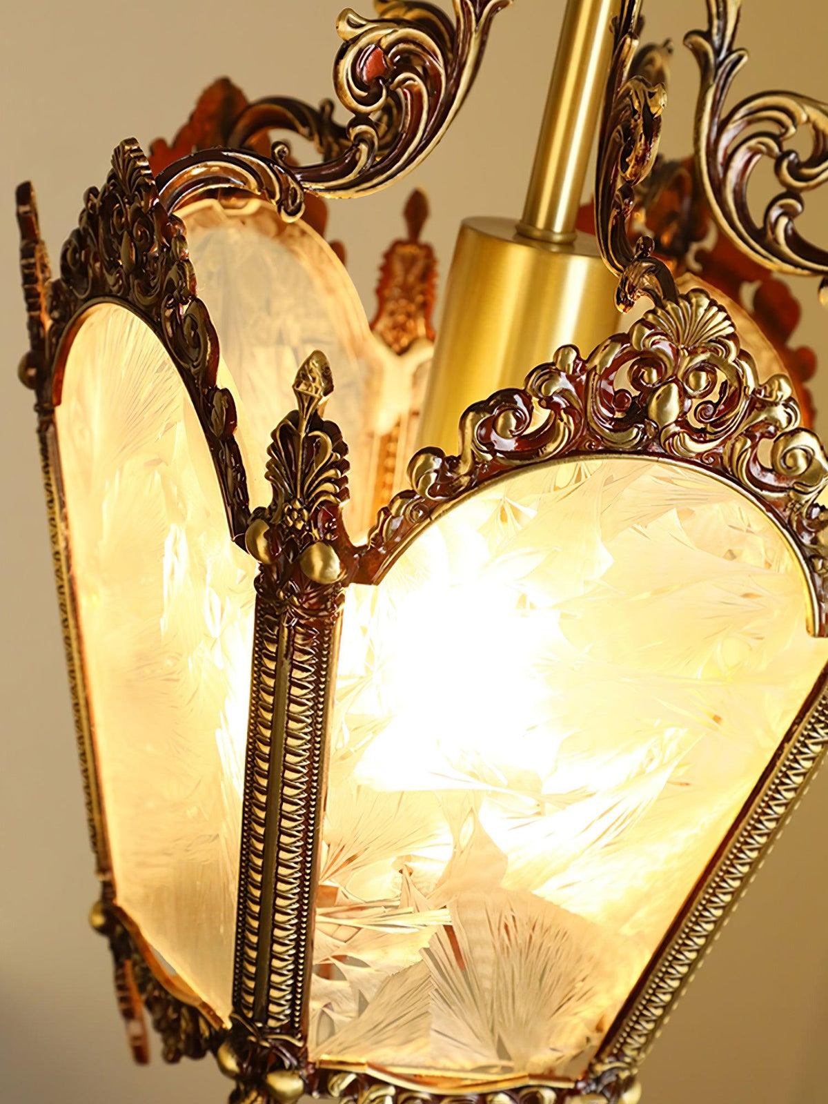 Lit Clérachic lantern pendant seen close, the amber glow visible through frosted panes and ornate brass edging.