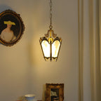 Lit brass lantern pendant hung near a curtain, with a gilt-framed portrait and a teacup below, from Clérachic.