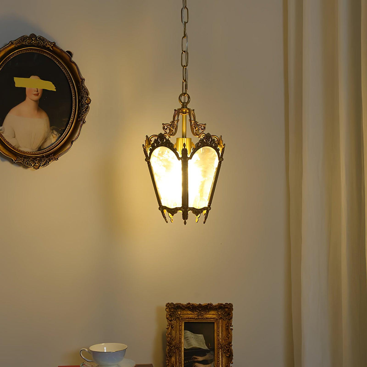 Lit brass lantern pendant hung near a curtain, with a gilt-framed portrait and a teacup below, from Clérachic.