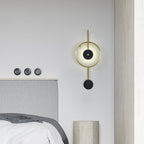 The Clérachic Orphaa mounted above a grey upholstered headboard, its warm glow catching the travertine bedside pillar.