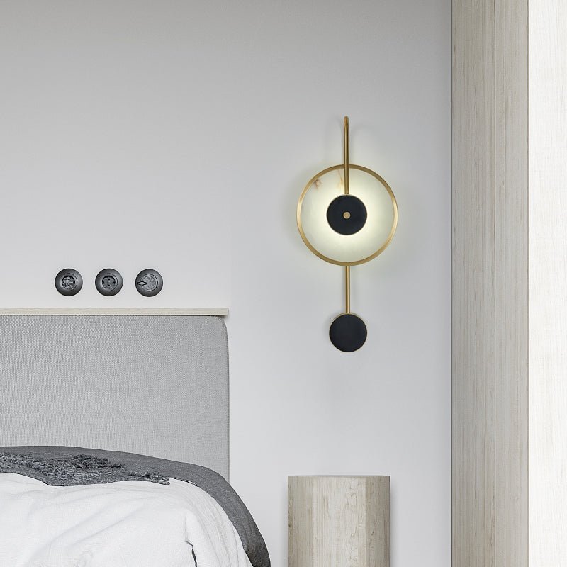 The Clérachic Orphaa mounted above a grey upholstered headboard, its warm glow catching the travertine bedside pillar.