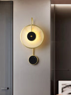 The Clérachic Orphaa beside a bronzed mirrored column, casting a soft halo over the greige wall.