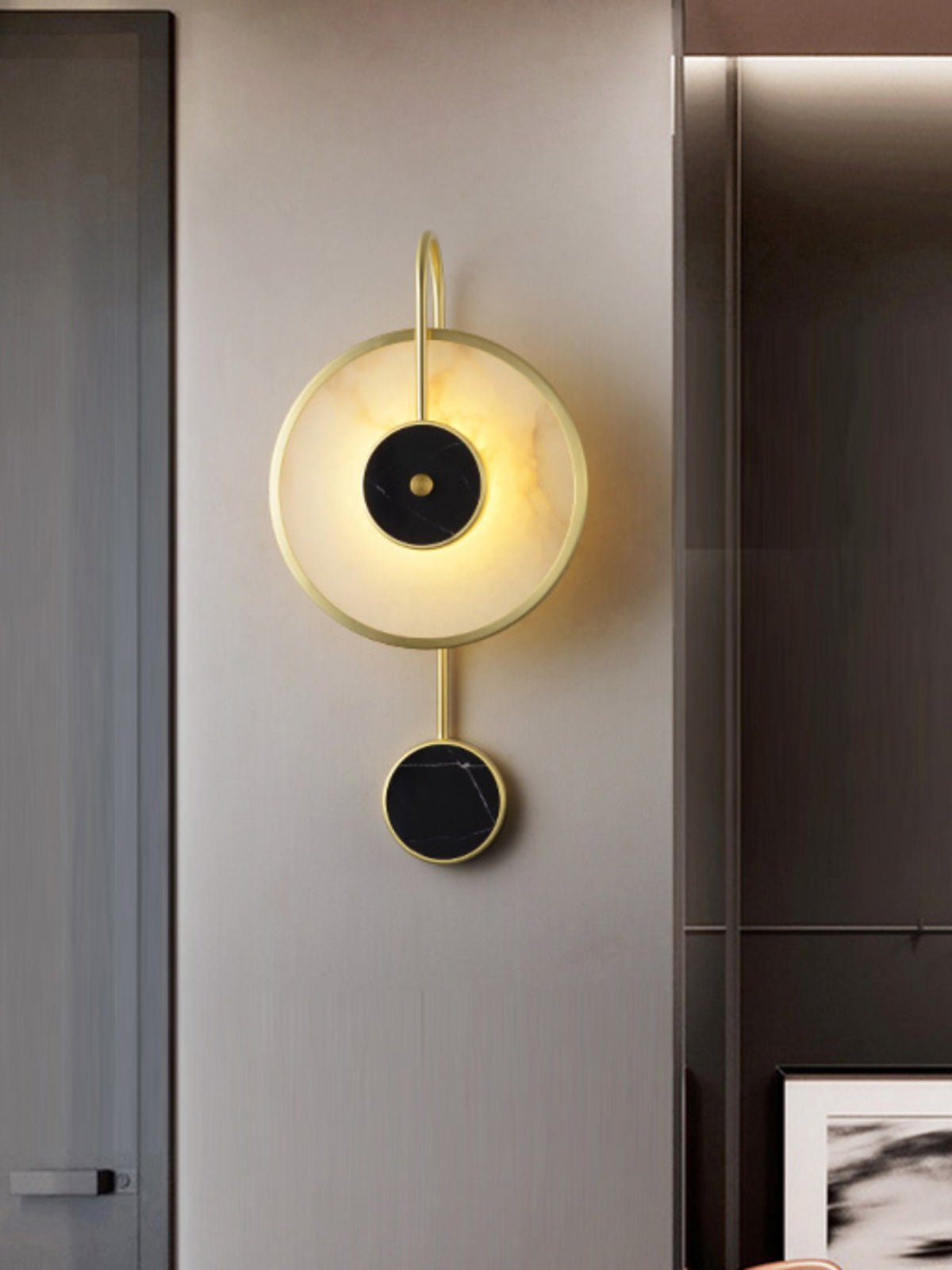 The Clérachic Orphaa beside a bronzed mirrored column, casting a soft halo over the greige wall.