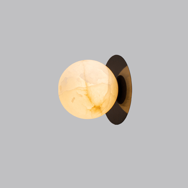 The Clérachic Orrila sconce in black finish, warm-lit stone globe against a grey backdrop.
