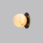 The Clérachic Orrila sconce in black finish, warm-lit stone globe against a grey backdrop.