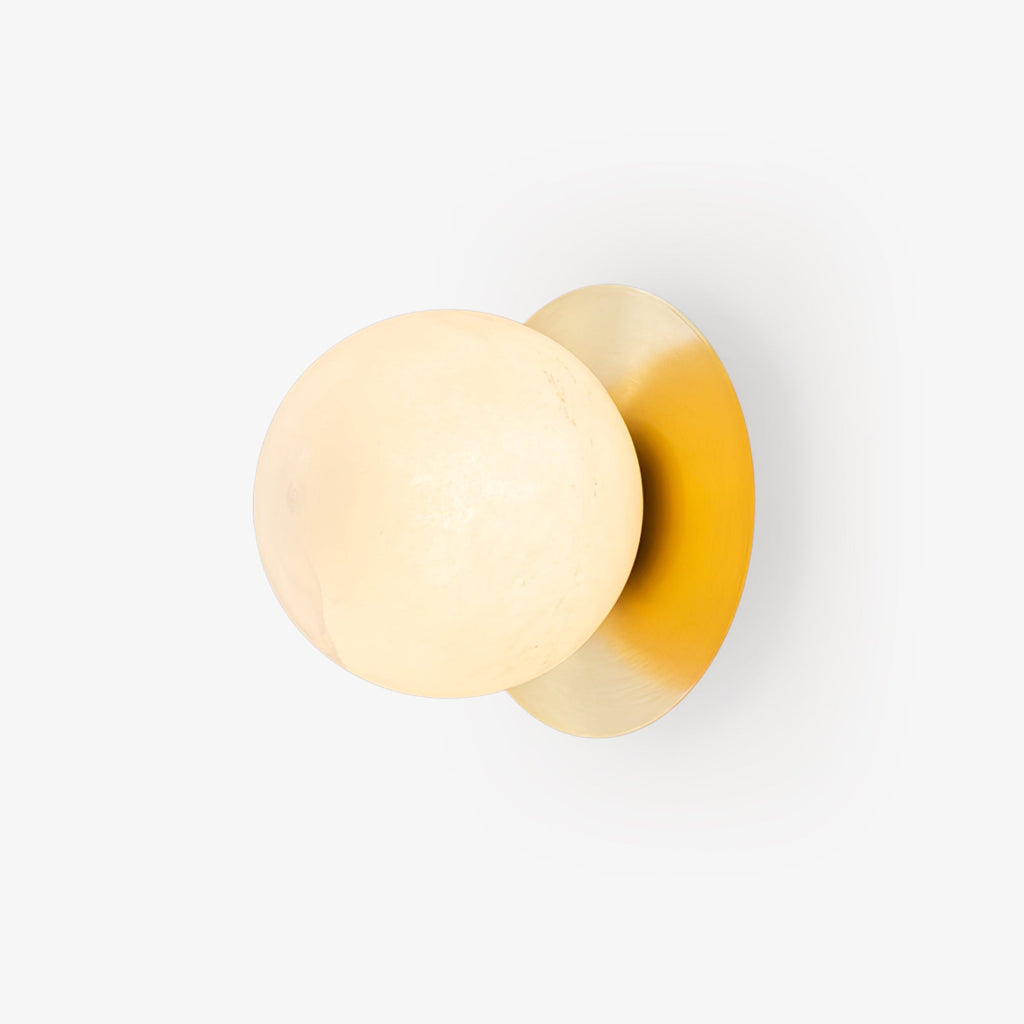 Clérachic Orrila wall light on pale grey, brass disc angled behind the glowing globe.