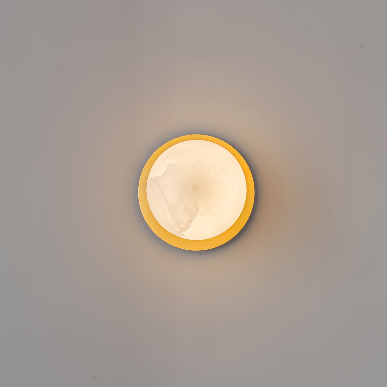 Clérachic Orrila wall light lit head-on, a ring of brass framing the alabaster face.