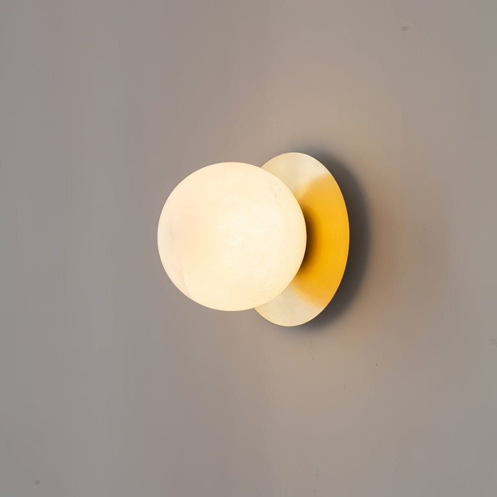 Clérachic Orrila wall sconce lit on grey, a soft shadow cast behind the brass plate.