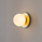 Clérachic Orrila wall sconce lit on grey, a soft shadow cast behind the brass plate.