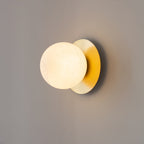 The Clérachic Orrila sconce angled on a grey wall, globe glowing beside the brass disc.