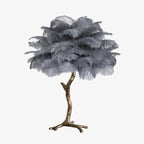 Clérachic table lamp with layered grey ostrich feathers on a bronze-toned branch stem and splayed feet, on a plain white background.