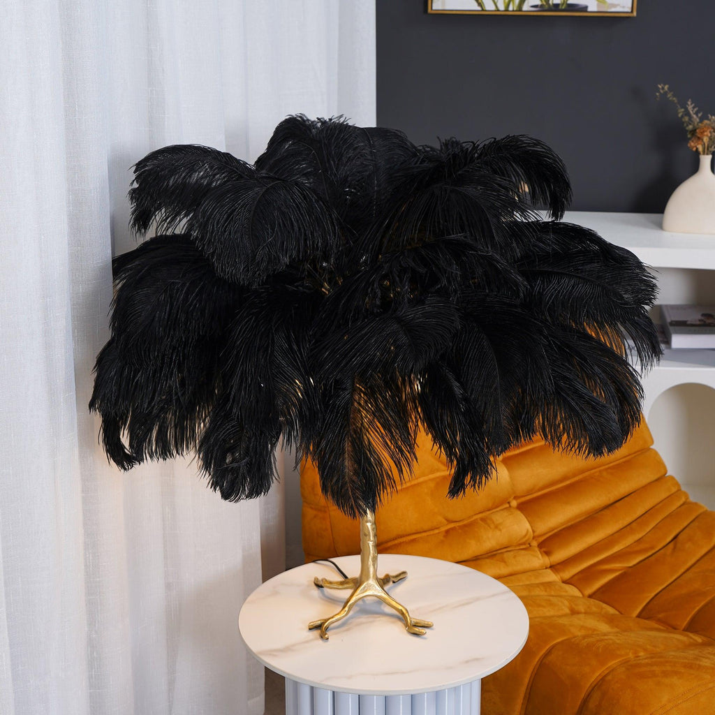 Close view of the black ostrich feather shade on this Clérachic table lamp, on a white fluted table in front of a mustard chair.