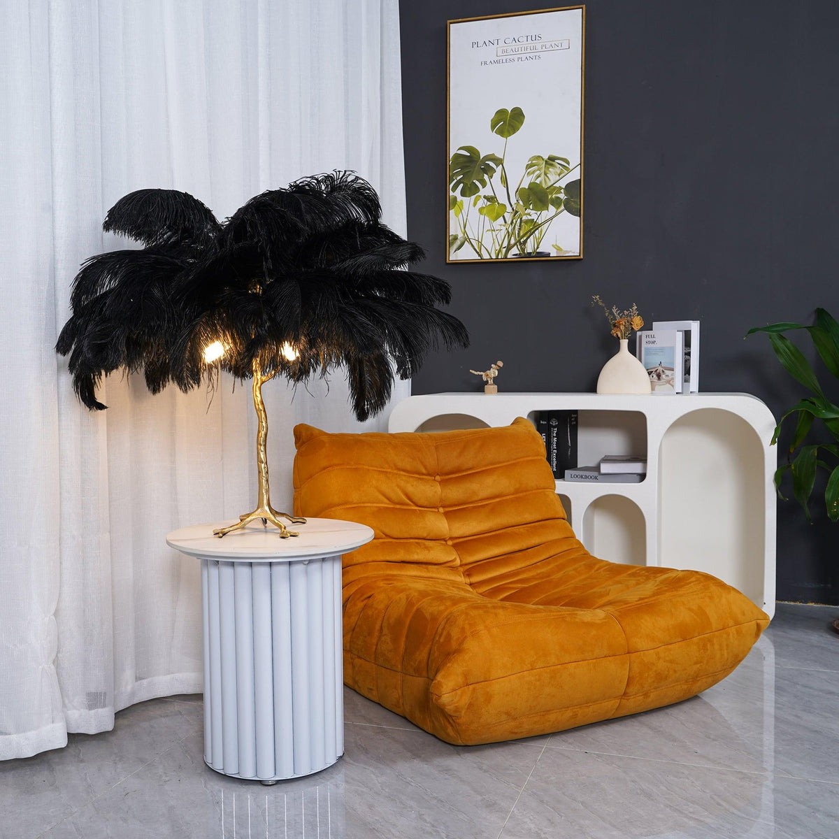 Clérachic black feather table lamp lit on a white fluted side table beside a mustard lounge chair, with a framed plant print above.