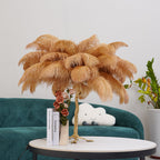 Clérachic table lamp with camel-coloured feathers on a round table with a vase of roses and books, in front of a green velvet sofa.