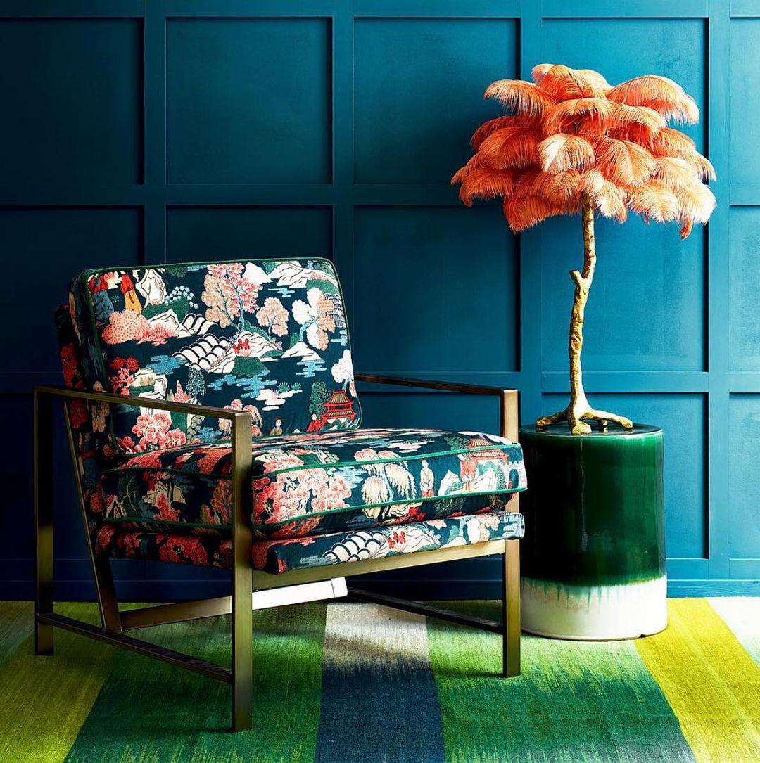 Clérachic table lamp with orange feathers on a green ceramic stool, beside a floral armchair in front of a teal panelled wall.