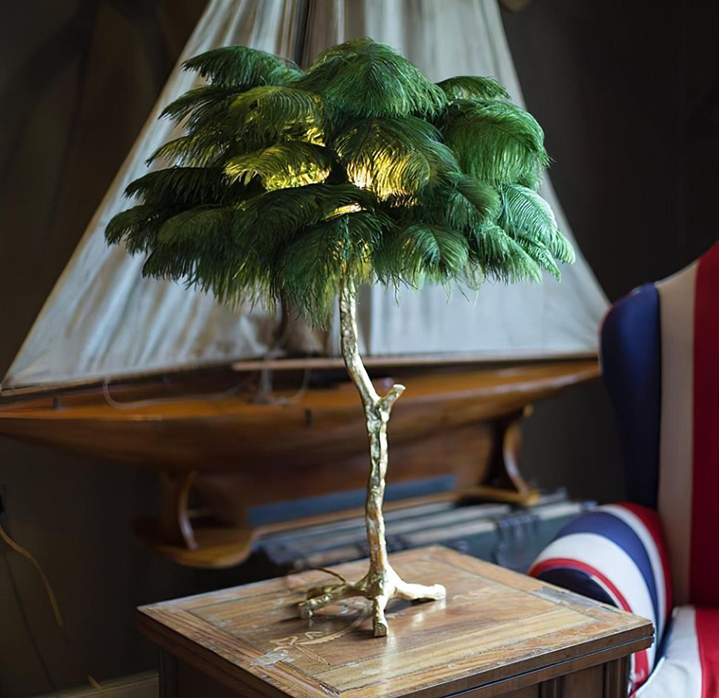 Clérachic table lamp with deep green ostrich feathers on a wooden side table, in front of a model sailing boat and a Union Jack chair.