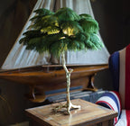 Clérachic table lamp with deep green ostrich feathers on a wooden side table, in front of a model sailing boat and a Union Jack chair.