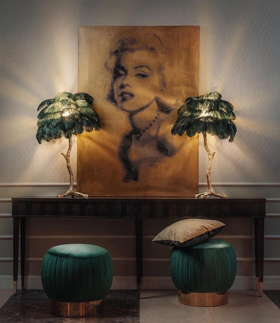 Two Clérachic feather lamps with dark green plumes on a dark console, on either side of a large portrait, with green velvet stools below.