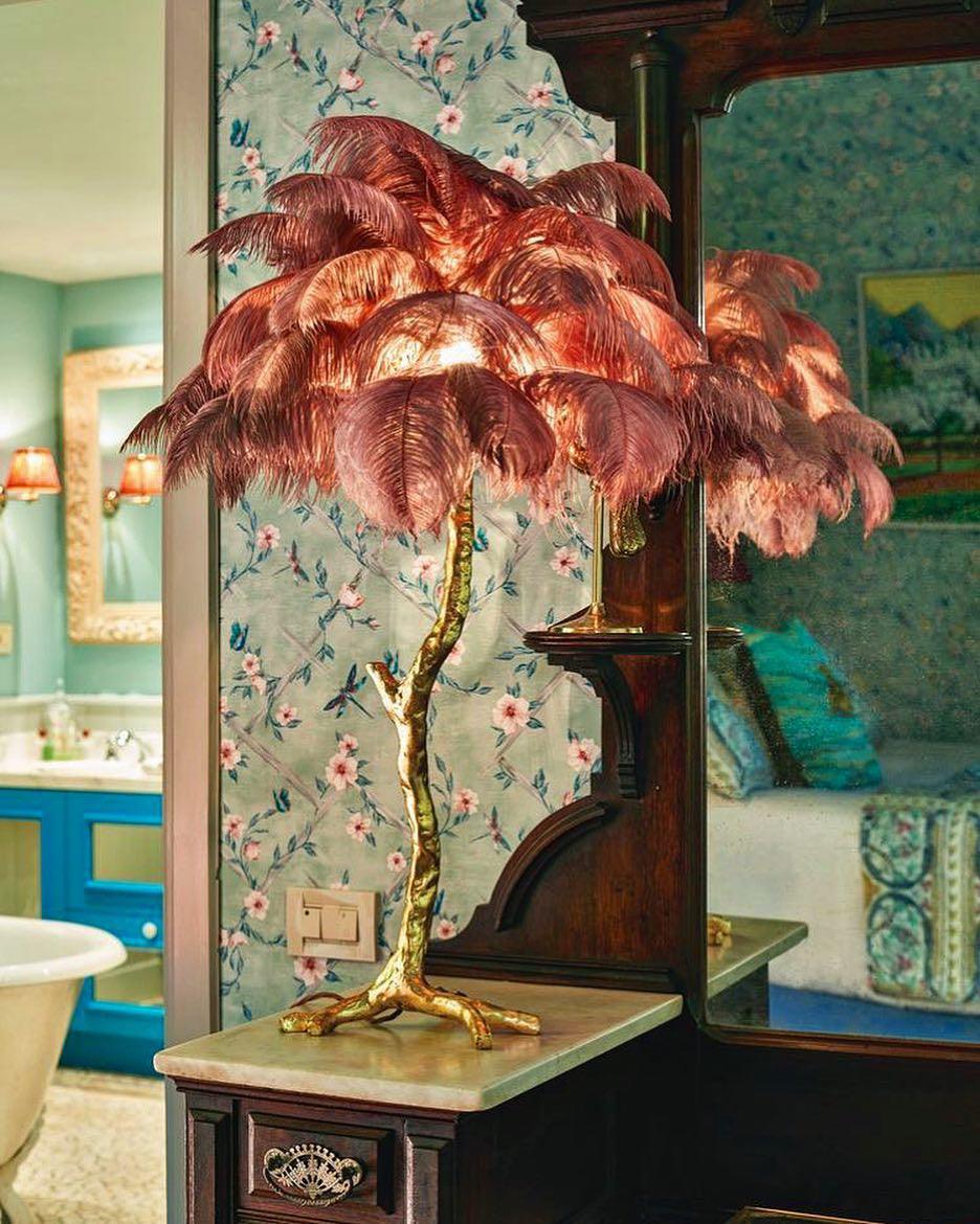 Clérachic feather lamp with rose-brown plumes lit on a marble-topped table, in a bathroom with floral wallpaper and a roll-top bath.