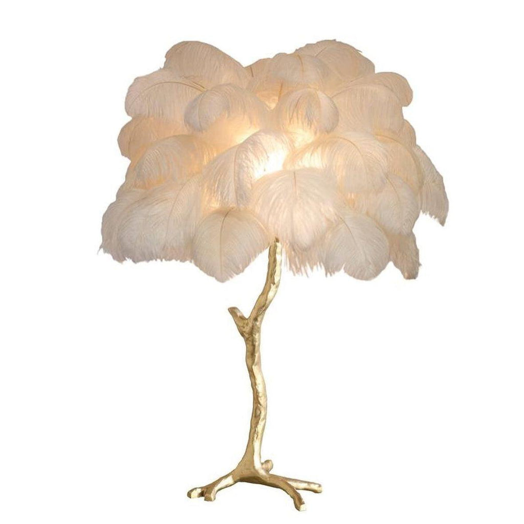 Clérachic table lamp with a lit cream-white feather shade on a gold branch stem, shown on a plain white background.