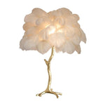 Clérachic table lamp with a lit cream-white feather shade on a gold branch stem, shown on a plain white background.