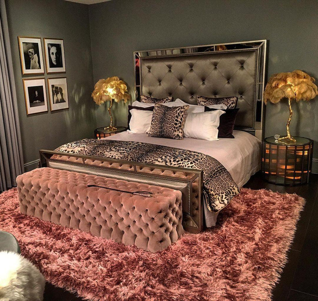 Two Clérachic feather lamps with gold plumes on the bedside tables of a bed with a leopard-print runner and a pink velvet bench.