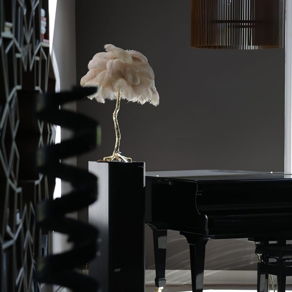 Small Clérachic feather lamp with pale pink plumes on a dark plinth in a grey room, with a black grand piano beside it.