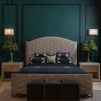 Two small Clérachic feather lamps with green plumes on bedside tables, either side of a quilted headboard on a deep teal wall.
