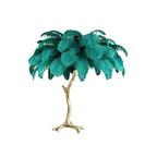 Clérachic table lamp with bright teal-green feathers on a gold branch stem, on a plain white background.