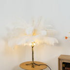 Clérachic feather lamp with white plumes lit from below on a round wooden table, in front of a pale wall and a wooden cabinet.