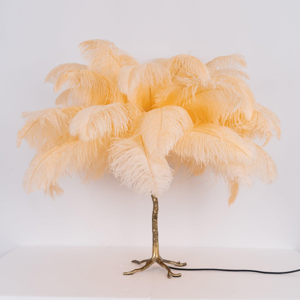 Clérachic table lamp with unlit peach-cream feathers on a gold branch stem and splayed feet, on a white surface.