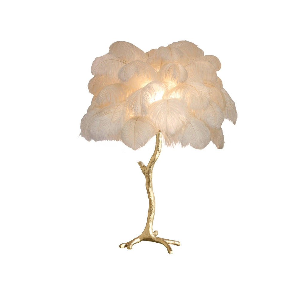 Clérachic table lamp with lit cream-white feathers on a gold branch stem with splayed feet, on a plain white background.