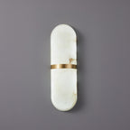 The Clérachic Ostruvyd pill sconce in white alabaster with a brushed brass band, mounted unlit on a soft grey-lilac wall.