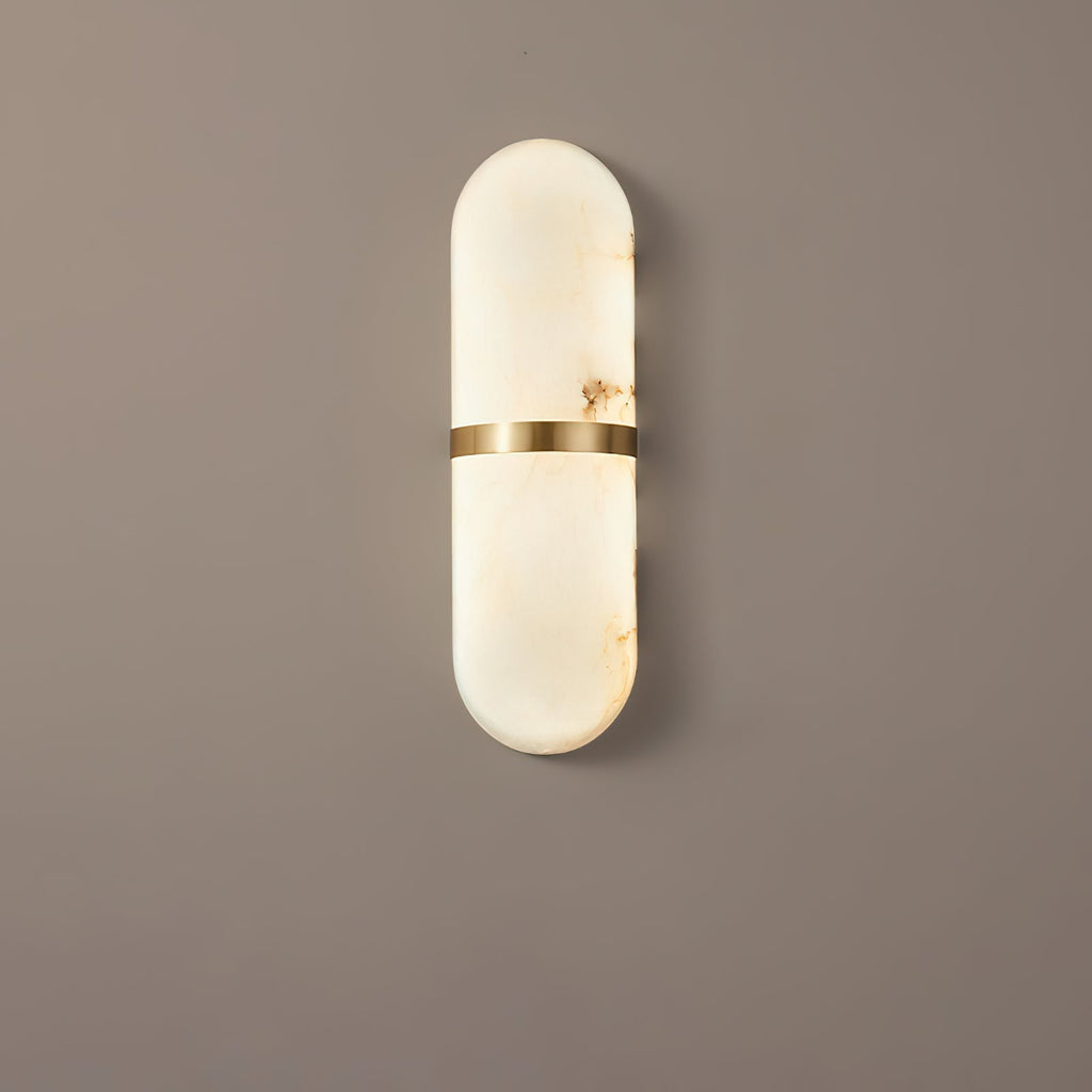 Clérachic alabaster wall lamp seen straight on against a warm taupe wall, its brass centre band splitting the pill in two.