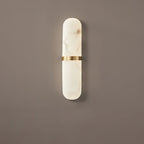 The Clérachic Ostruvyd in its slimmer size, pale alabaster and brass, casting a soft shadow down a mocha-brown wall.