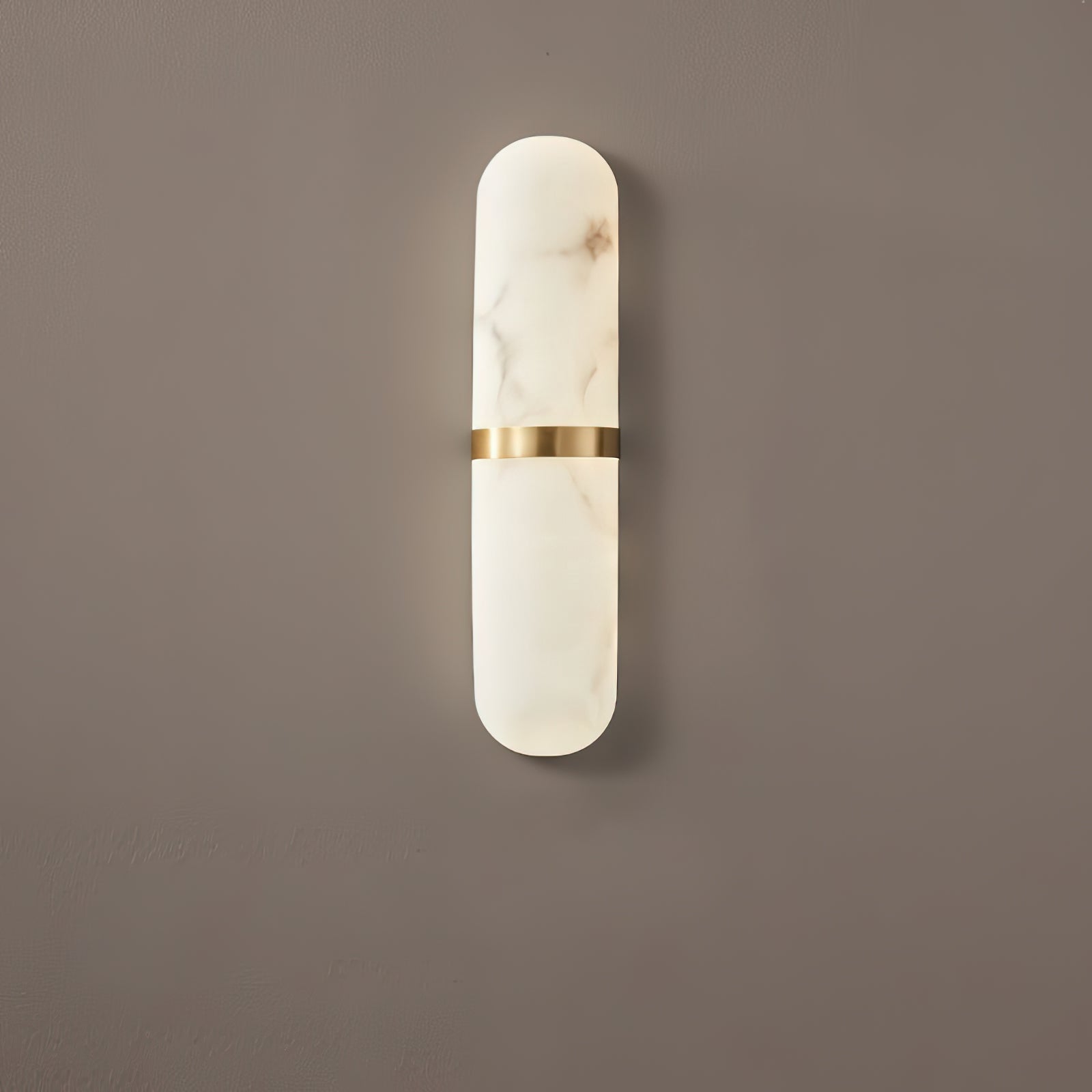 The Clérachic Ostruvyd in its slimmer size, pale alabaster and brass, casting a soft shadow down a mocha-brown wall.
