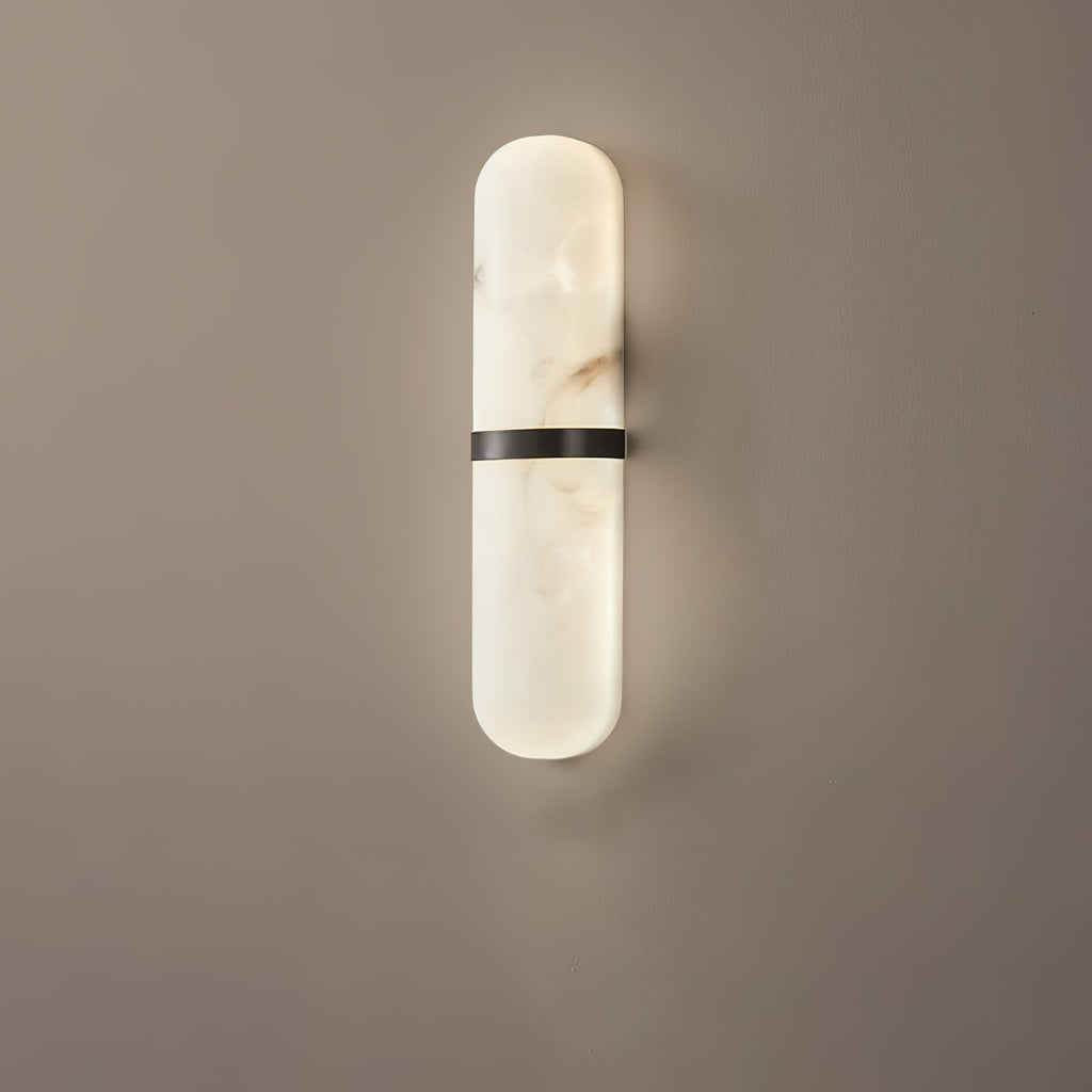 Clérachic pill sconce in the black-banded finish, matte metal set against veined alabaster on a warm greige wall.