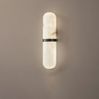 Clérachic pill sconce in the black-banded finish, matte metal set against veined alabaster on a warm greige wall.