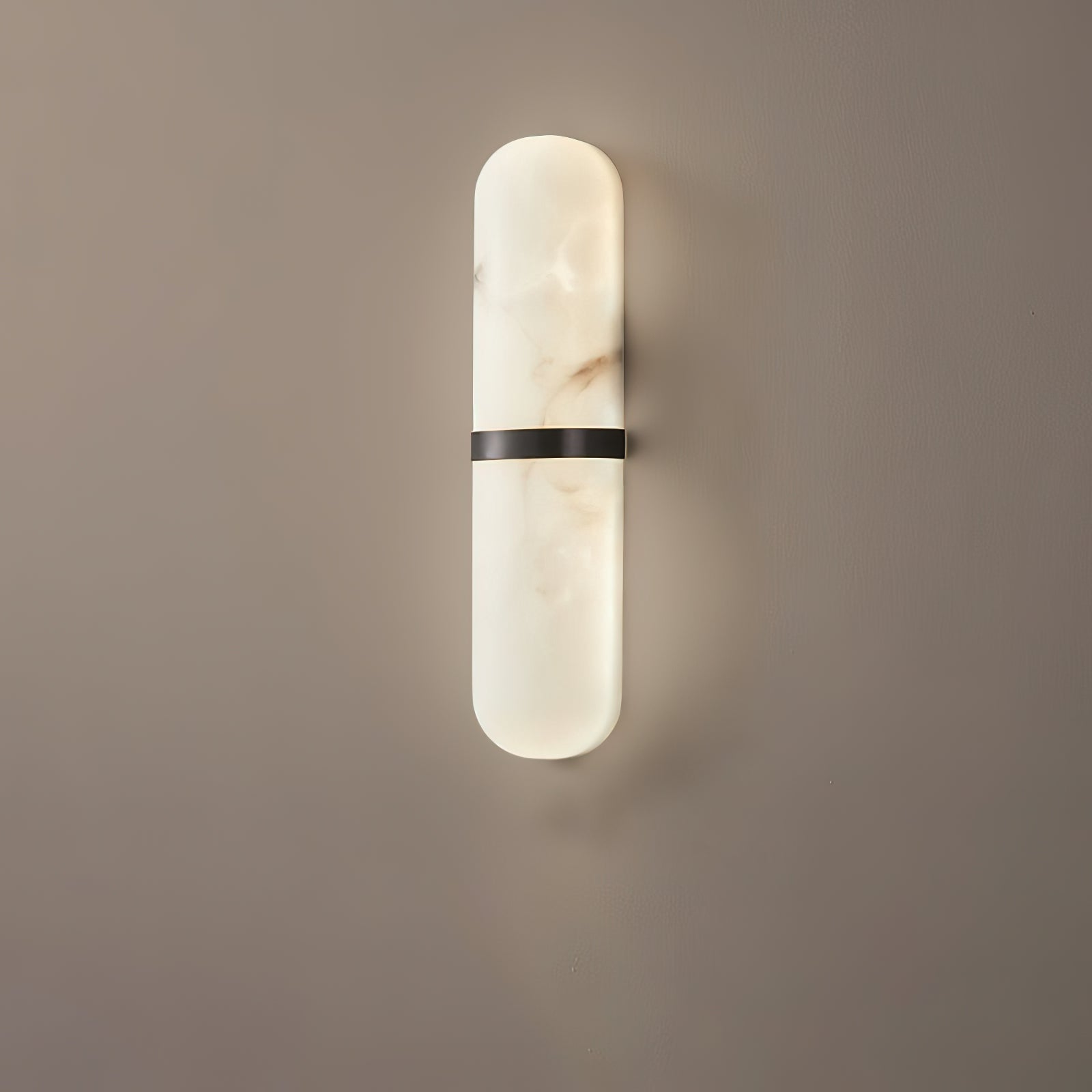 Clérachic pill sconce in the black-banded finish, matte metal set against veined alabaster on a warm greige wall.