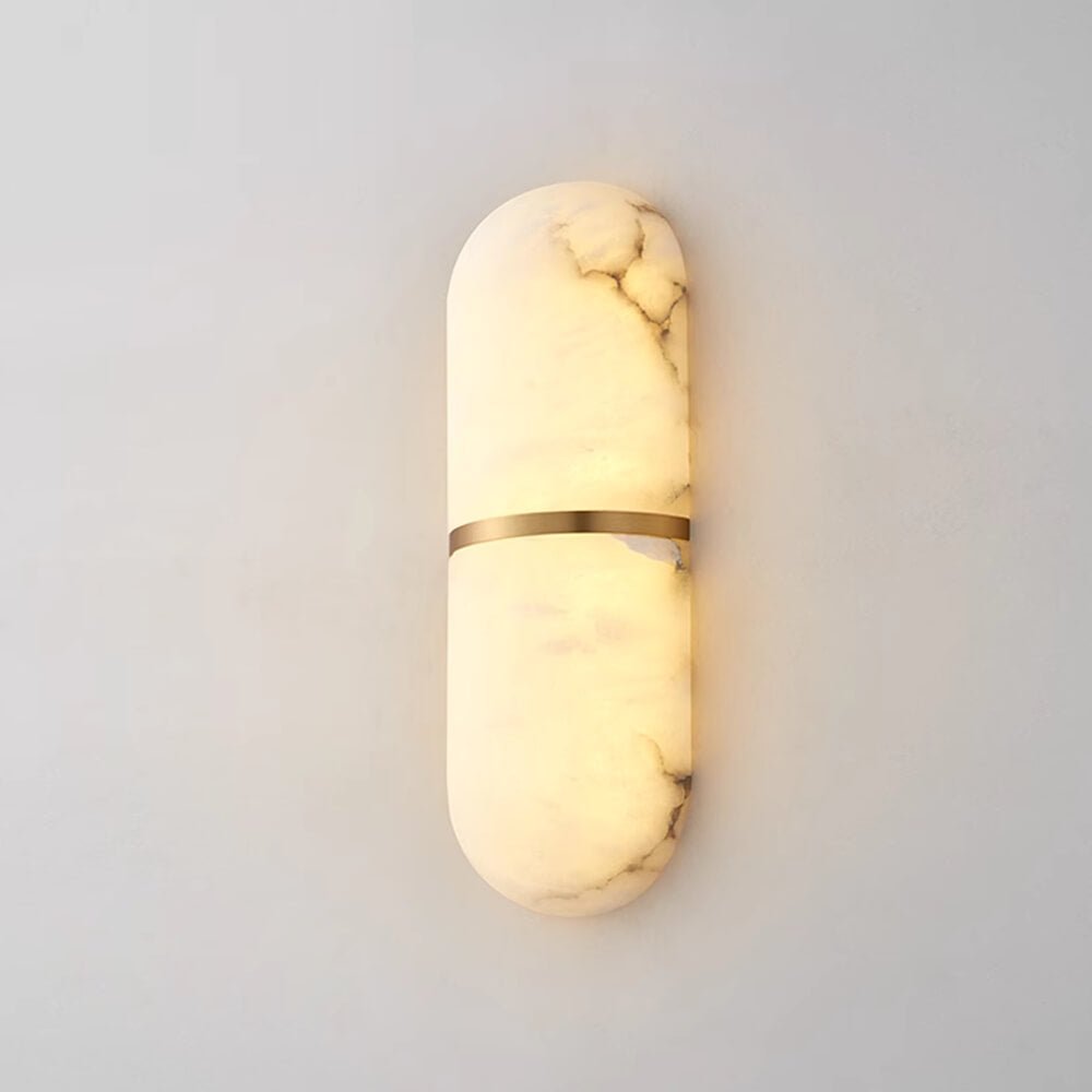 The Clérachic wall lamp lit, alabaster glowing amber through its natural veining above a pale plaster wall.