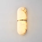 The Clérachic wall lamp lit, alabaster glowing amber through its natural veining above a pale plaster wall.